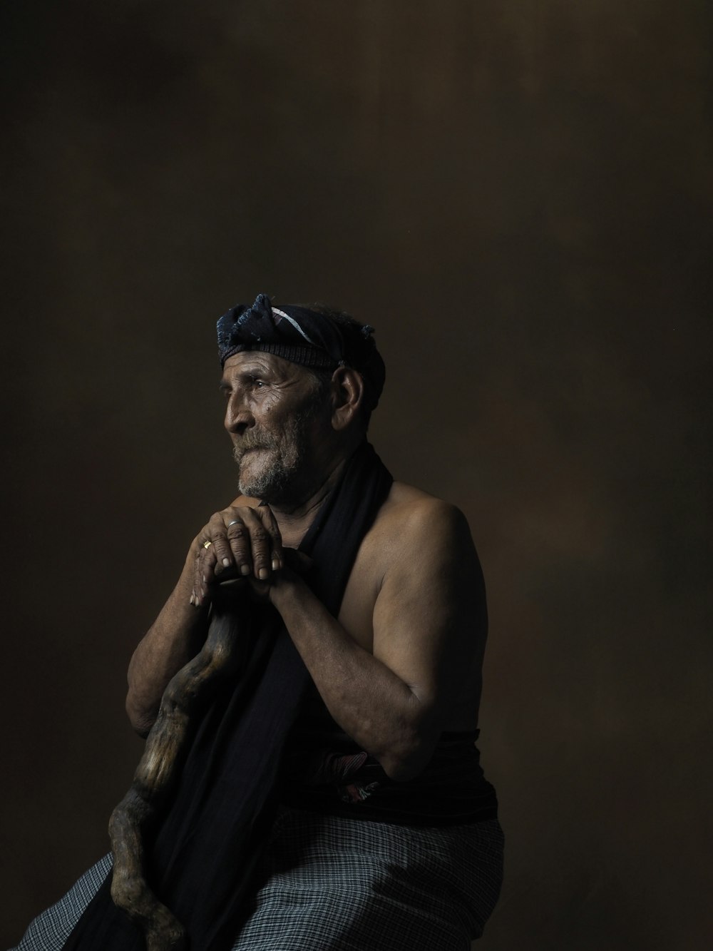 topless man sitting against brown wall