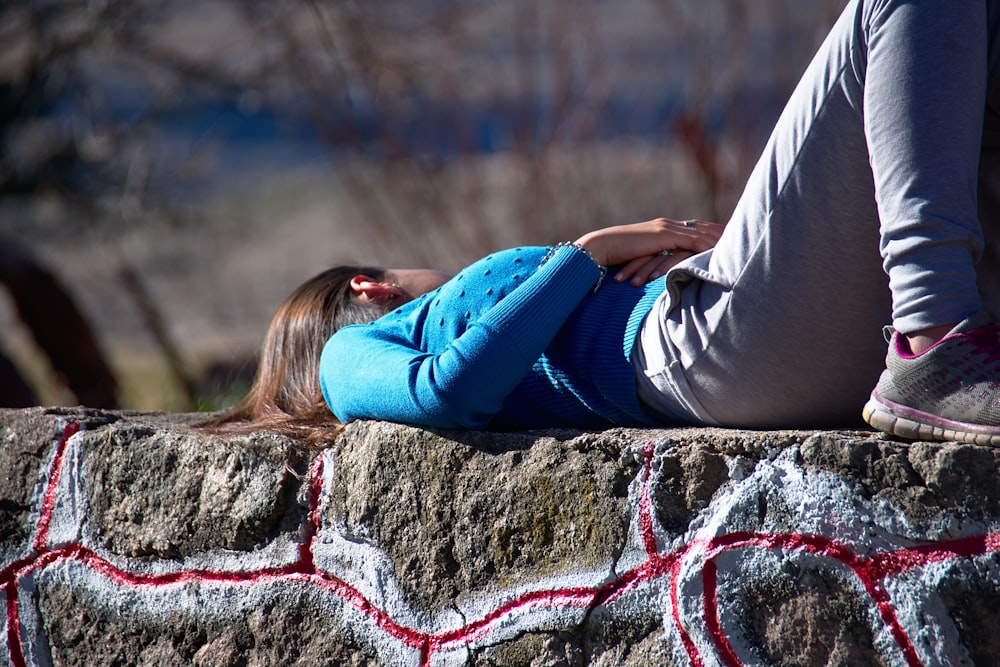 파란색 긴팔 상의와 회색 운동복 바지를 입은 여자가 콘크리트 표면에 누워 있습니다.