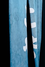 A close-up view of blue fabric or curtains featuring white lettering or symbols partially visible against a dark background.