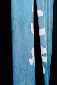 A close-up view of blue fabric or curtains featuring white lettering or symbols partially visible against a dark background.