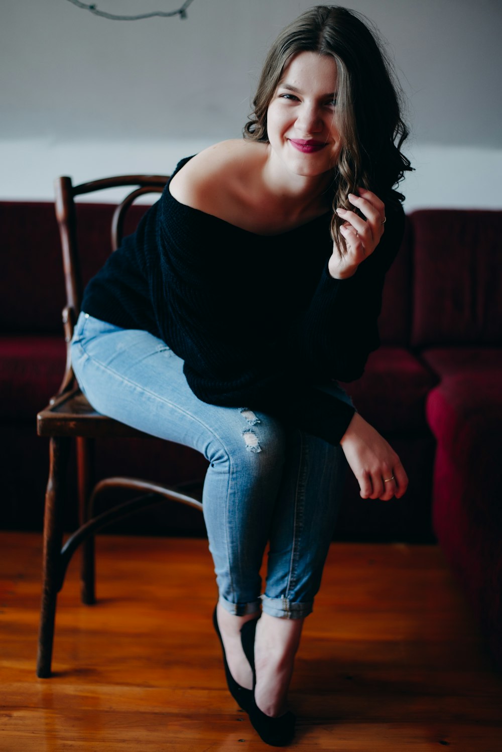 smiling woman wearing black off-shoulder long sleeved shirt with blue denim jeans sitting on chair