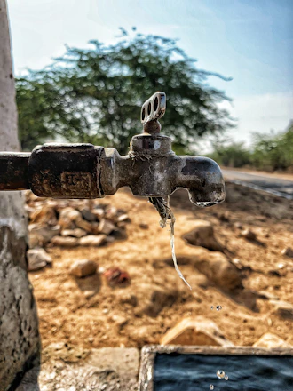 A close-up of a rusty water faucet dripping water in a dry neighborhood.