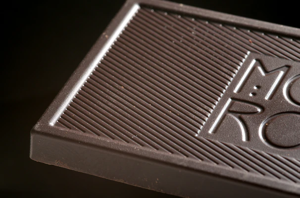 Close-up of a glossy dark chocolate bar with delicate gold leaf accents on a matte black surface.