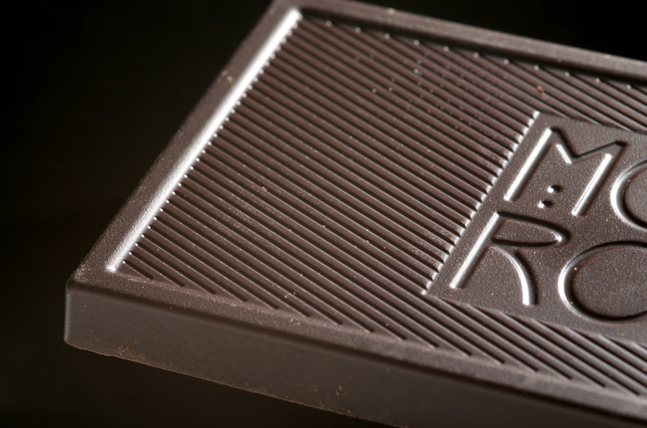 Close-up of a luxurious dark chocolate bar with delicate gold leaf accents on a rich wooden surface.