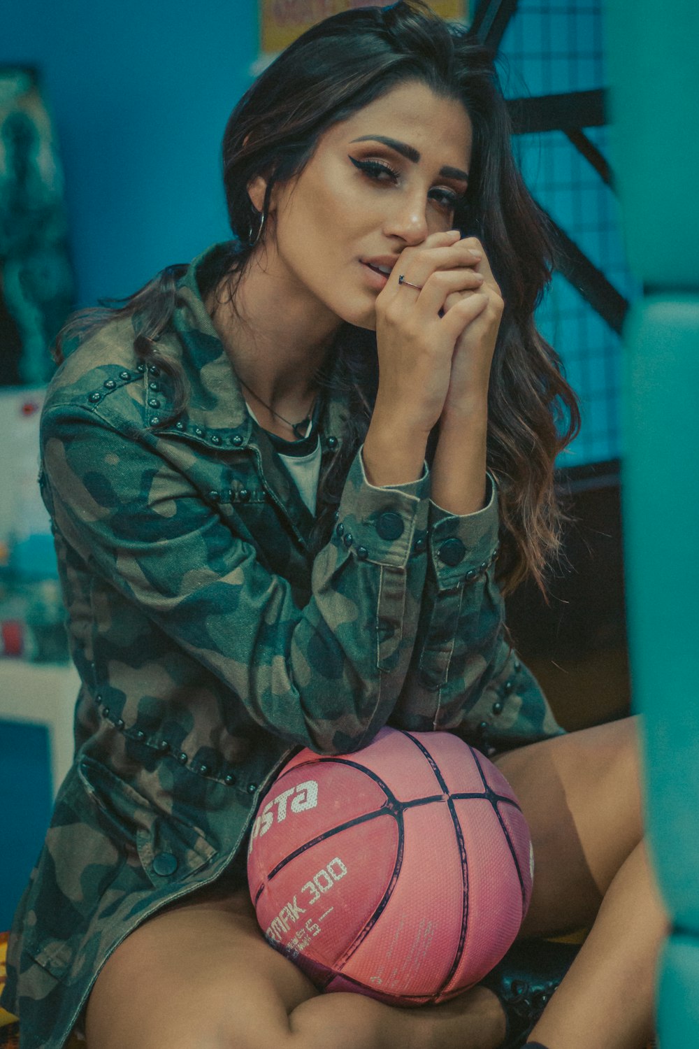 mujer con chaqueta de camuflaje que apoya el codo en la pelota de baloncesto en el regazo