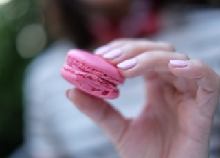 selective focus photography of person holding pink cookie