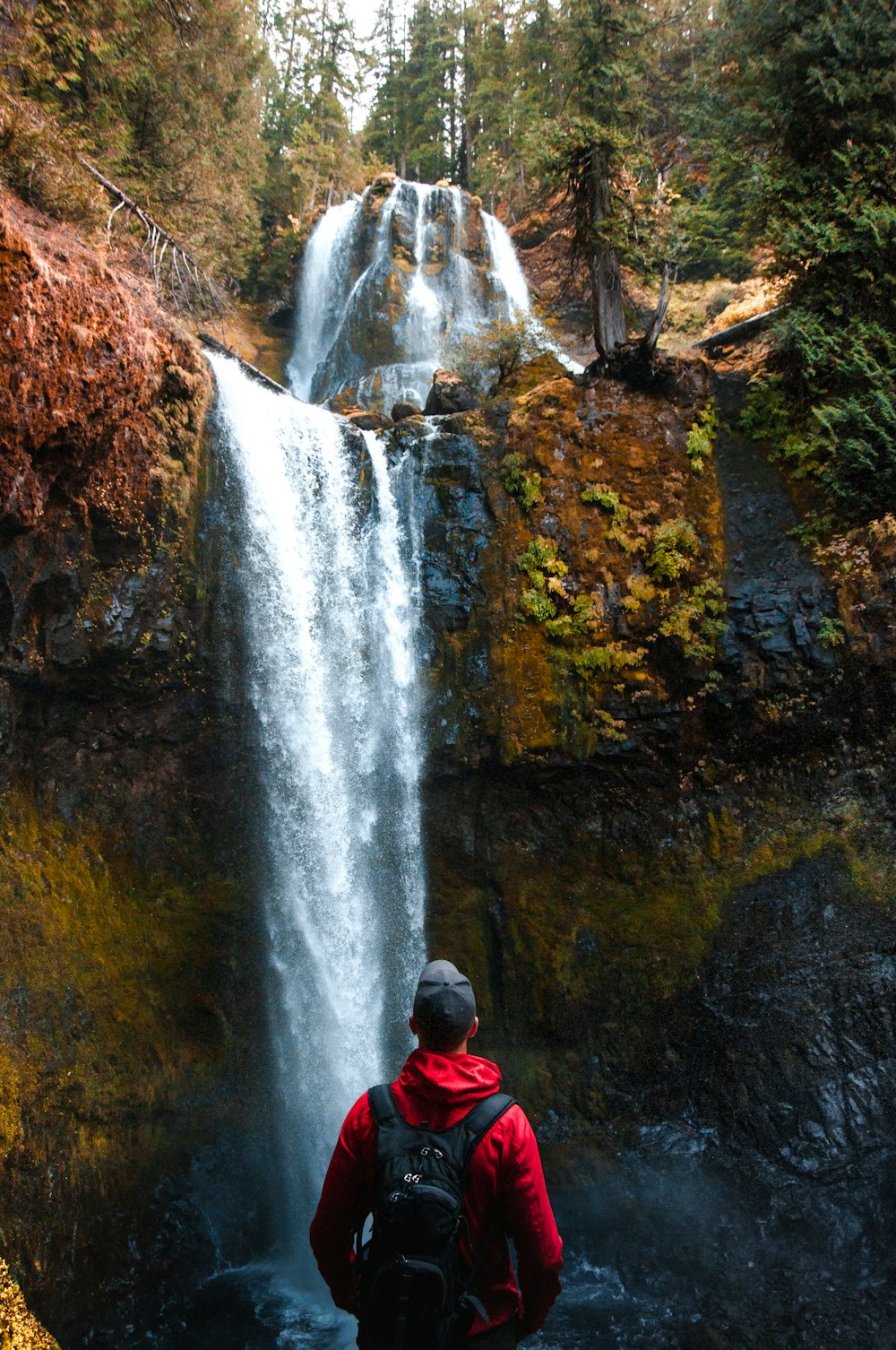 man wearing red jacket watching waterfalls