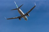 A commercial airplane is captured mid-flight against a clear blue sky. The aircraft is seen from below, highlighting its wings and engines.