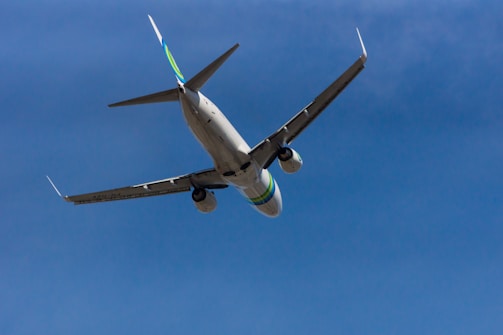 A commercial airplane is captured mid-flight against a clear blue sky. The aircraft is seen from below, highlighting its wings and engines.