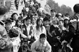 A large group of people, including adults and children, walk along a crowded section of what appears to be a historic stone structure. Many are wearing jackets and carrying bags, and some are taking photos.