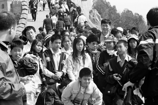 A large group of people, including adults and children, walk along a crowded section of what appears to be a historic stone structure. Many are wearing jackets and carrying bags, and some are taking photos.