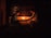 Two individuals are seated across from each other in a dimly lit room, with a warm glow from candles on a table between them. They appear to be engaged in a quiet, intimate conversation or activity. The wooden background suggests a rustic or traditional setting.