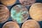 Several coins are displayed on a dark, textured background. Most of the coins have a golden-brown metallic appearance and include embossed text and numbers. One coin, in the center, appears heavily corroded and shows greenish oxidation, contrasting with the others.