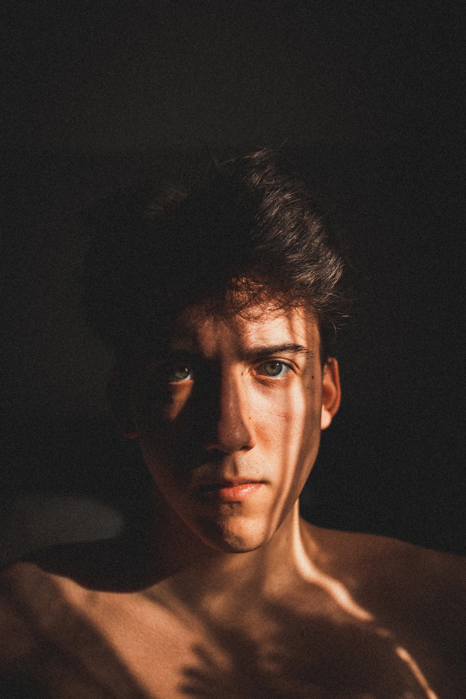 Young man casts shadow on black wall as light source illuminates his face