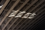 Curved metal beams create a pattern of arches with light casting across them, highlighting the texture and structure. The rivets and shadows accentuate the industrial design.