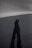 A long shadow of a person stretches across a smooth, featureless, and dark landscape under diffused lighting conditions.