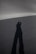 A long shadow of a person stretches across a smooth, featureless, and dark landscape under diffused lighting conditions.