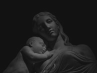 Softly lit marble figure of a mother cradling her baby, evoking timeless love and care.