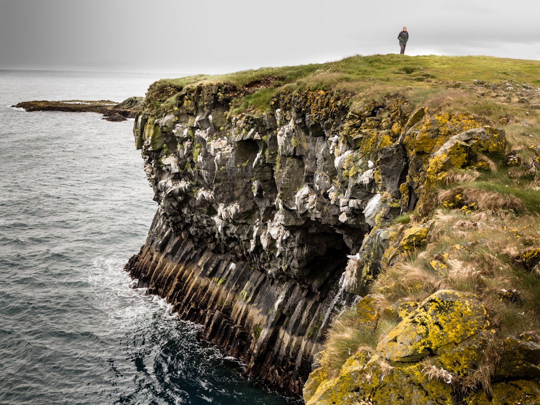 person standing on cliff near body of water,
