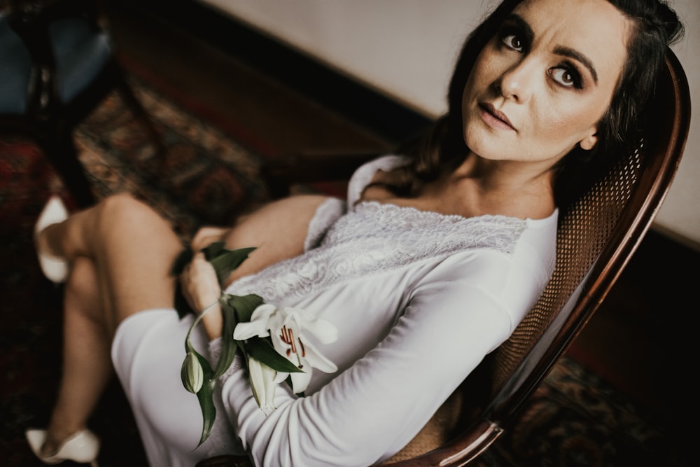 woman in white dress sits and holds flower