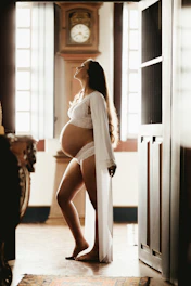 Pregnant woman gently stretching in a sunlit room with soft natural light.