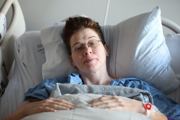 a white woman lying on a bed in hospital after surgery, looking hopeful