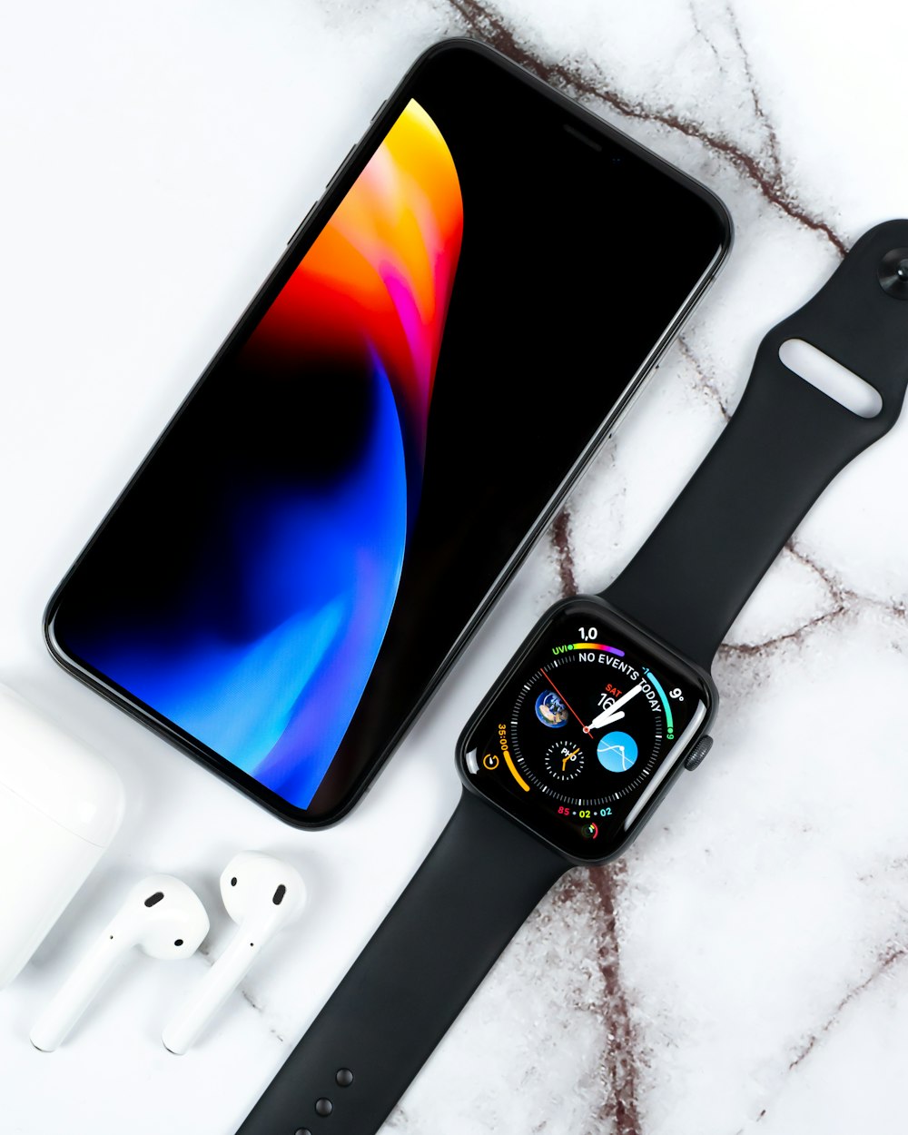 custodia in alluminio nero Apple Watch con cinturino sportivo nero e Apple AirPods su superficie bianca