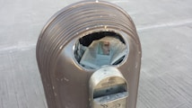A metallic trash can with a newspaper partially protruding from the opening. The newspaper displays a partially visible image of a face.