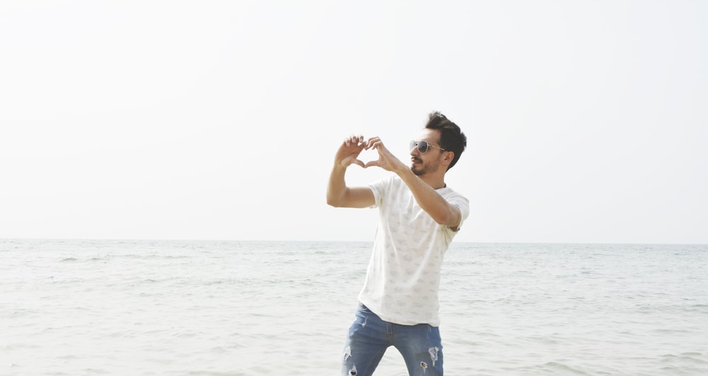 man in white t-shirt wearing sunglasses forming heart using both hands near s