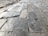 A close-up perspective of an uneven stone pavement, with rectangular stones laid out in a grid pattern. The surface has a mix of smoother and rougher textures with visible wear and aging, signifying use over time.
