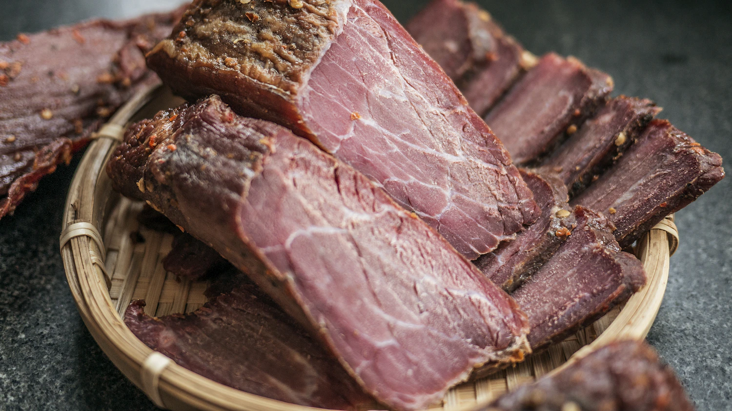 Slabs of dark smoked beef with a pink centre, stacked in a woven basket