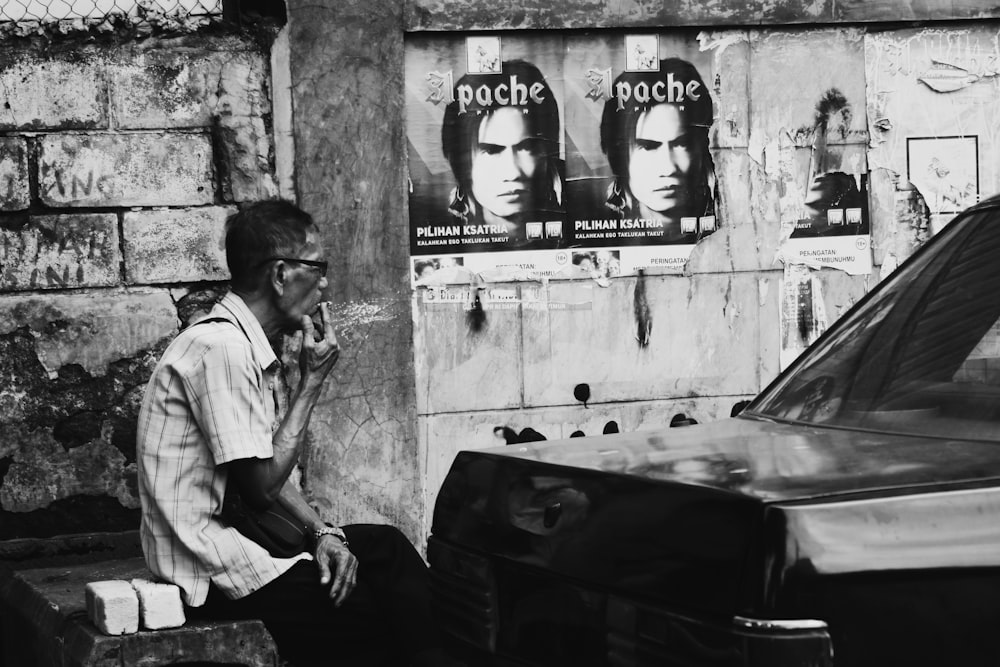 grayscale photography of man smoking near vehicle