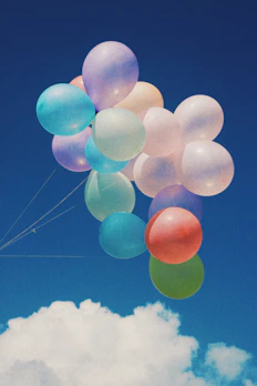 Colorful helium balloons floating against a clear blue sky.