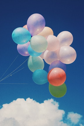 A close-up of hands releasing colorful balloons into a bright blue sky.