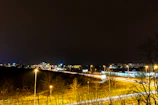 Nighttime shot of a semi-truck navigating a well-lit interstate with city lights in the background.