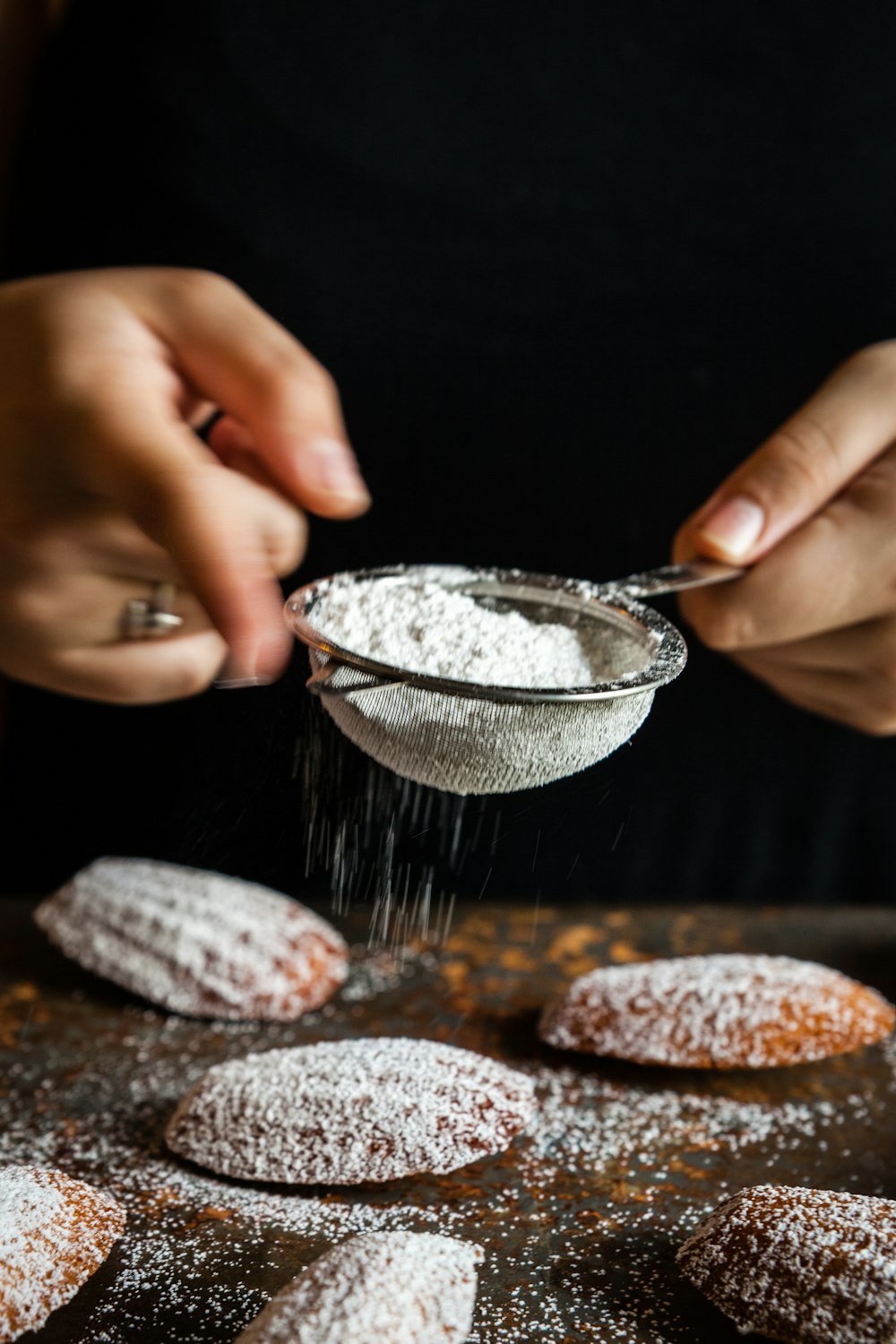 a person sprinkling powder on top of pastries