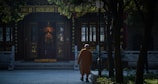 A person in traditional attire walks towards an ornate temple entrance, surrounded by trees casting shadows. The setting conveys a sense of serenity and retreat into a sacred space.