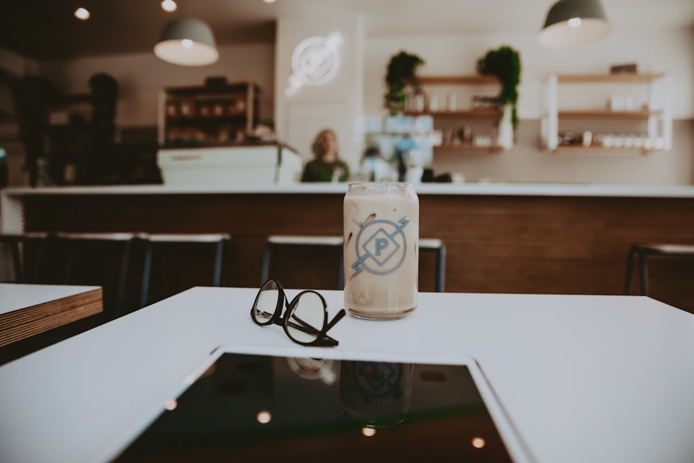 black framed eyeglasses beside glass cup on white wooden table