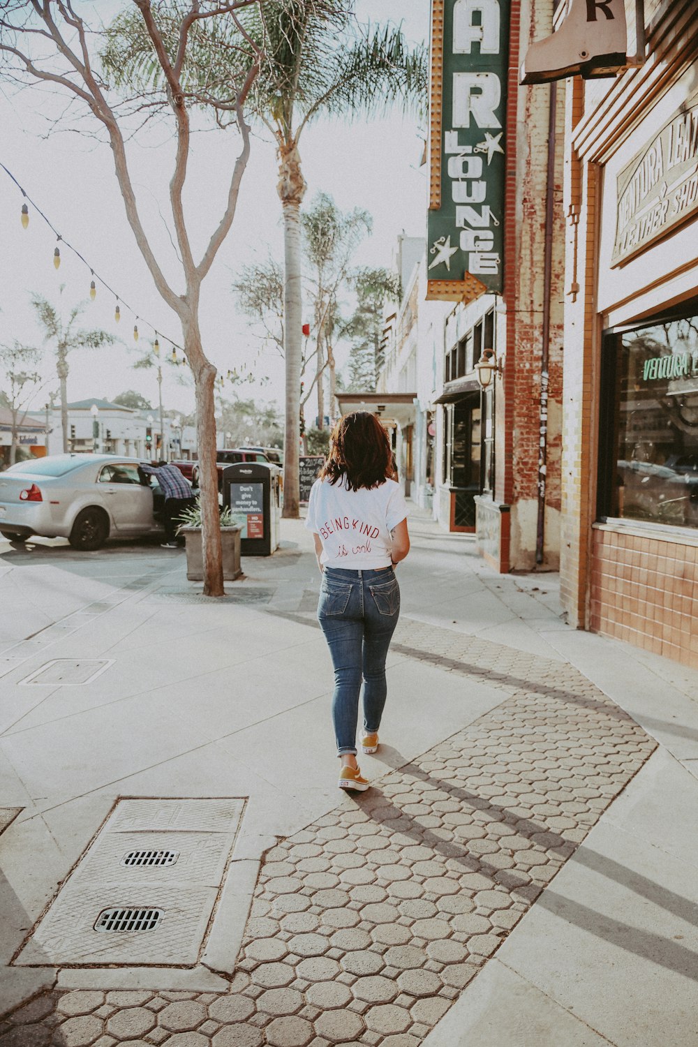 woman walking beside building and tree during daytime