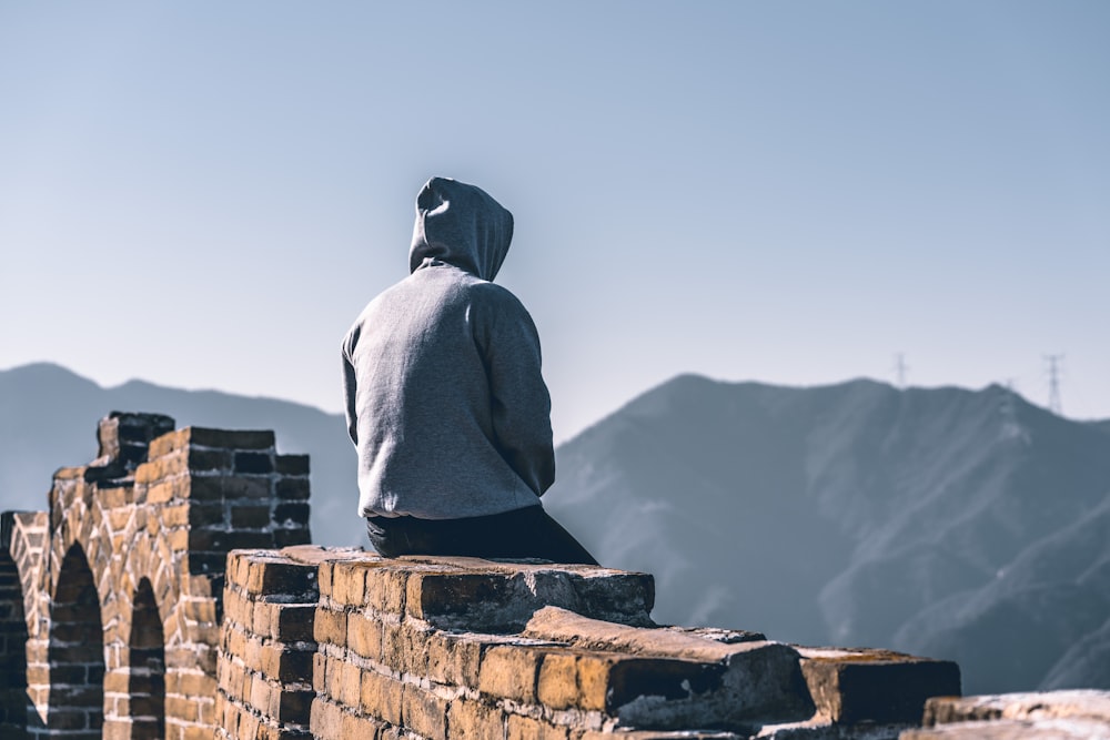 person in grey hoodie sitting on brick wall