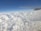 An airplane wing is visible against a backdrop of fluffy white clouds stretching across the sky. The vast expanse of clouds appears soft and dense, with a clear blue sky above.