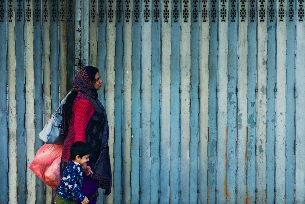 woman in black and red scarf holding boy beside gray building