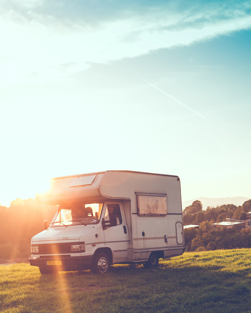 White camper van parked on grassy hill, basking in warm sunset glow outdoors