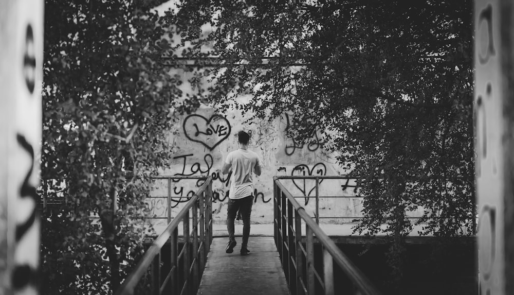grayscale photography of man standing on bridge