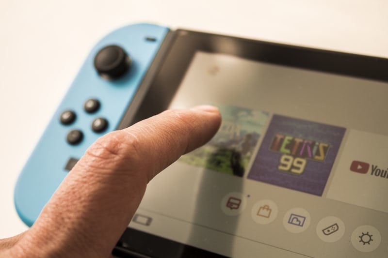 A hand holds a Nintendo Switch and selects a game