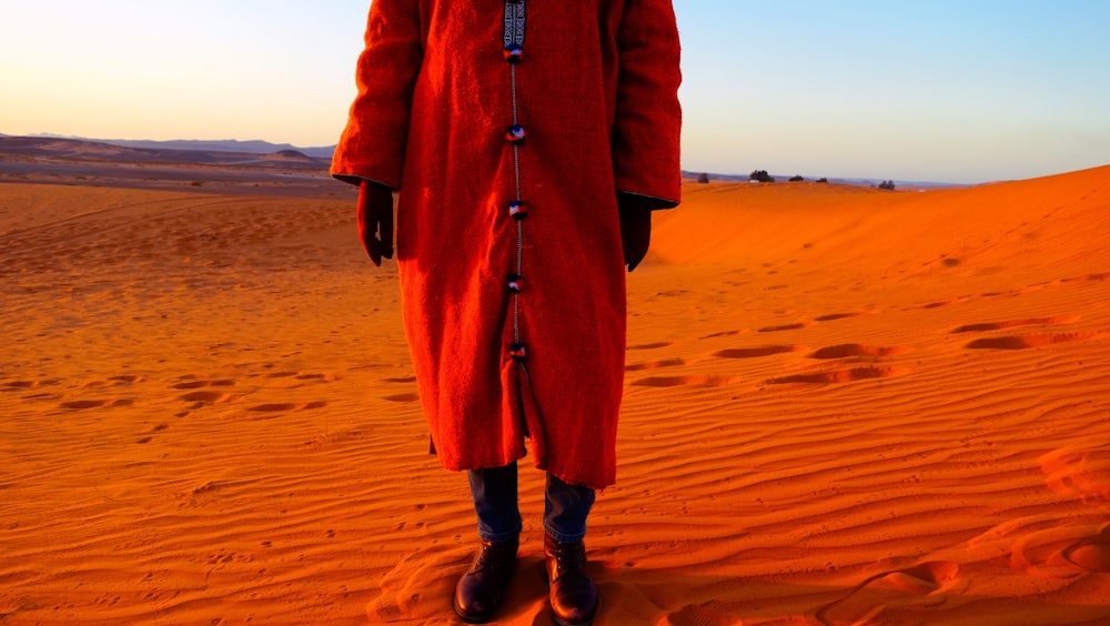 person wearing red coat standing on desert sands