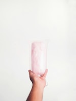 A hand is holding a large transparent cup filled with pink cotton candy against a plain white background.