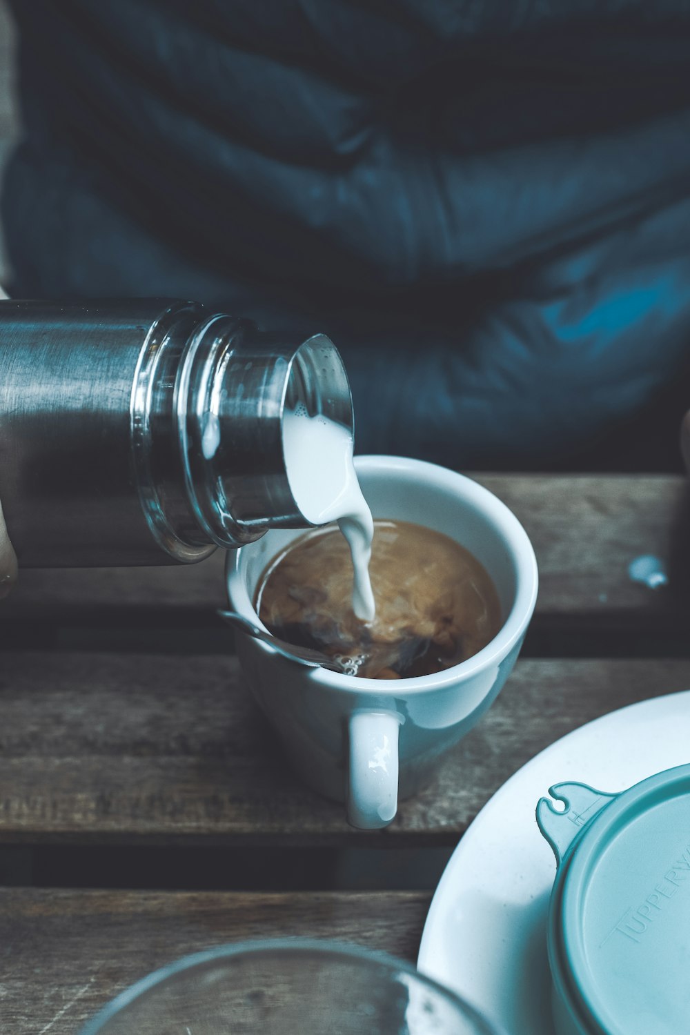 person pouring milk in coffee cup