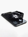 A sleek, black smartwatch with a sporty strap is resting on top of a black smartphone. The watch face displays the time with bold white numbers and additional information in smaller text. Both devices have a glossy finish that reflects light.