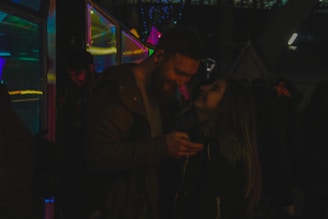 Smiling couple holding their instant photo strips, glowing under colorful event lights.